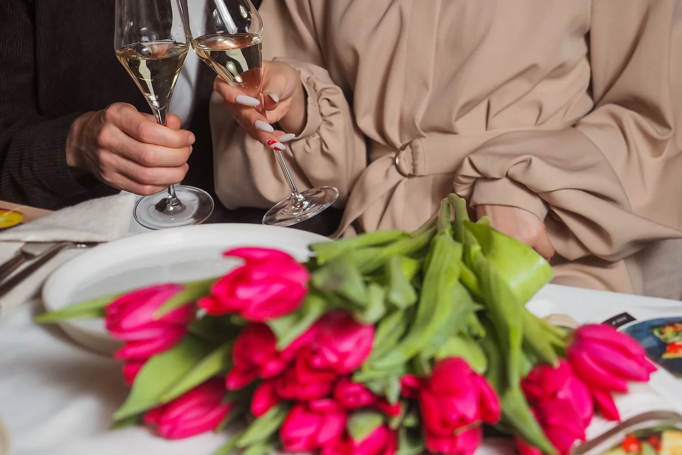 Přípitek dvěma sklenicemi sektu nad slavnostně prostřeným stolem s kyticí tulipánů